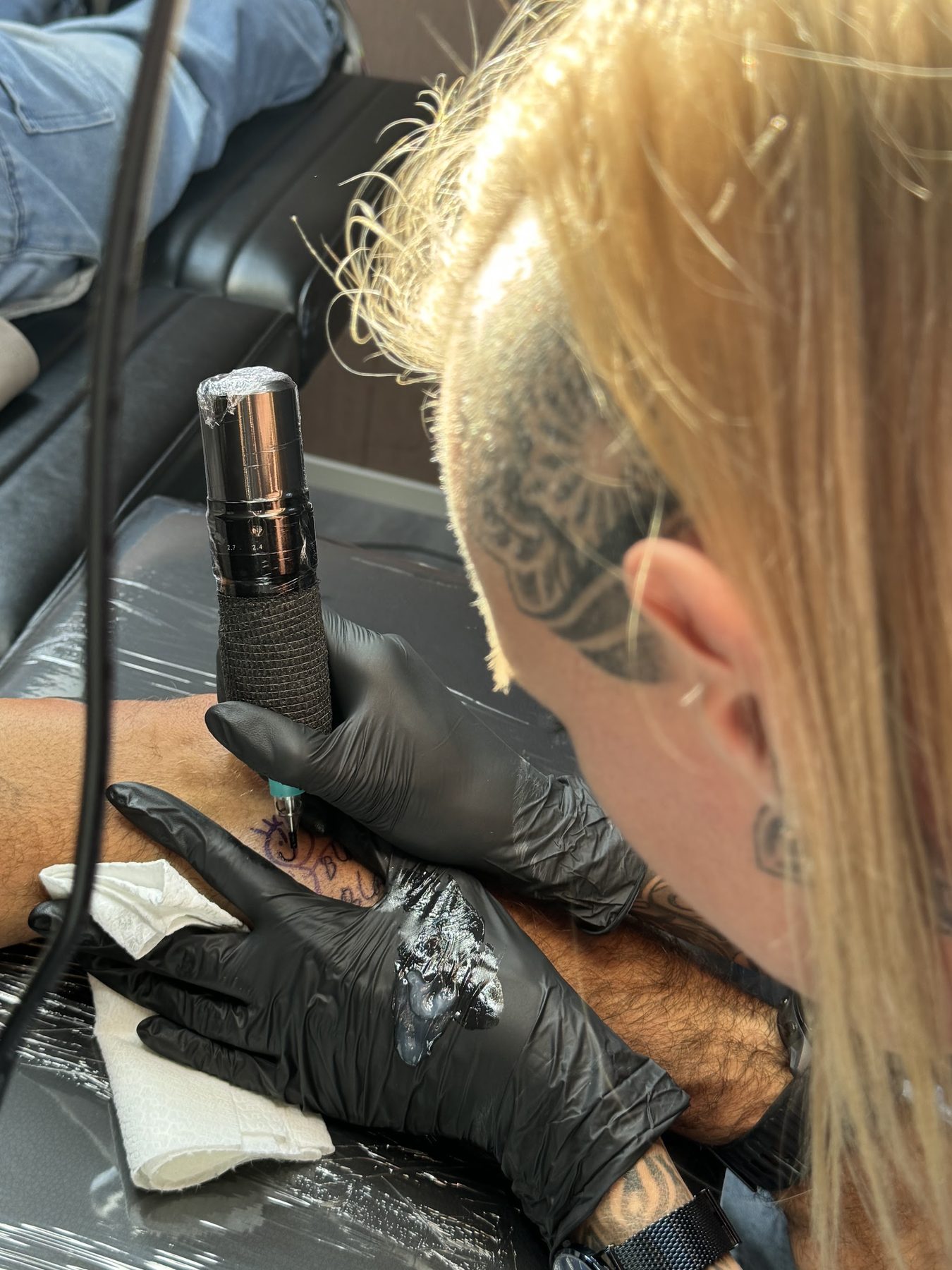 Kimberly aan het werk met de tattoomachine, in zwarte handschoenen